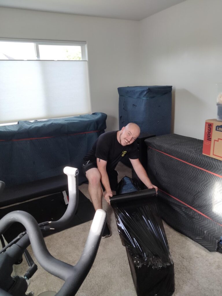 A man from All Smile Moving is lifting a large piece of furniture in a room, demonstrating careful handling.