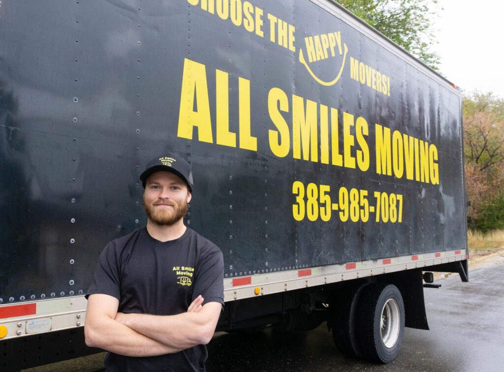 . A man stands in front of a moving truck labeled "All Smiles Moving," smiling and ready for the moving process