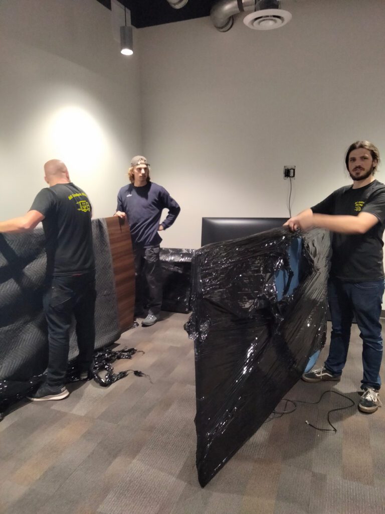 Three men from All Smile Moving collaborate on assembling a large piece of furniture in a well-lit workspace.