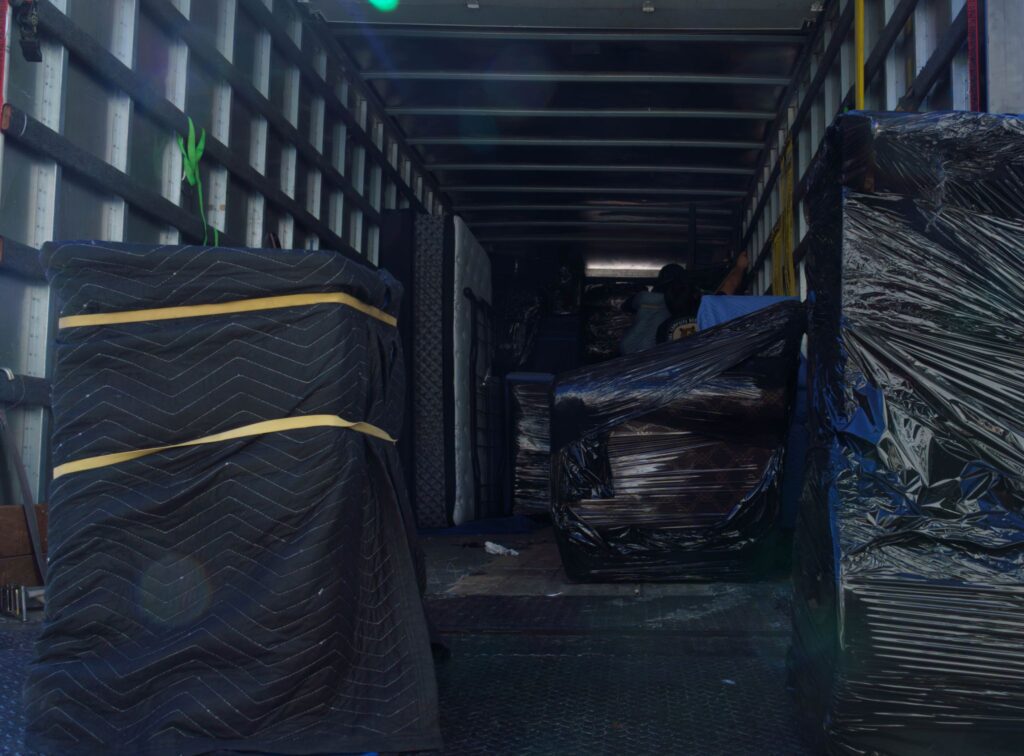 Interior view of a moving truck cargo bay filled with blanket-wrapped and plastic-shrink-wrapped furniture items.