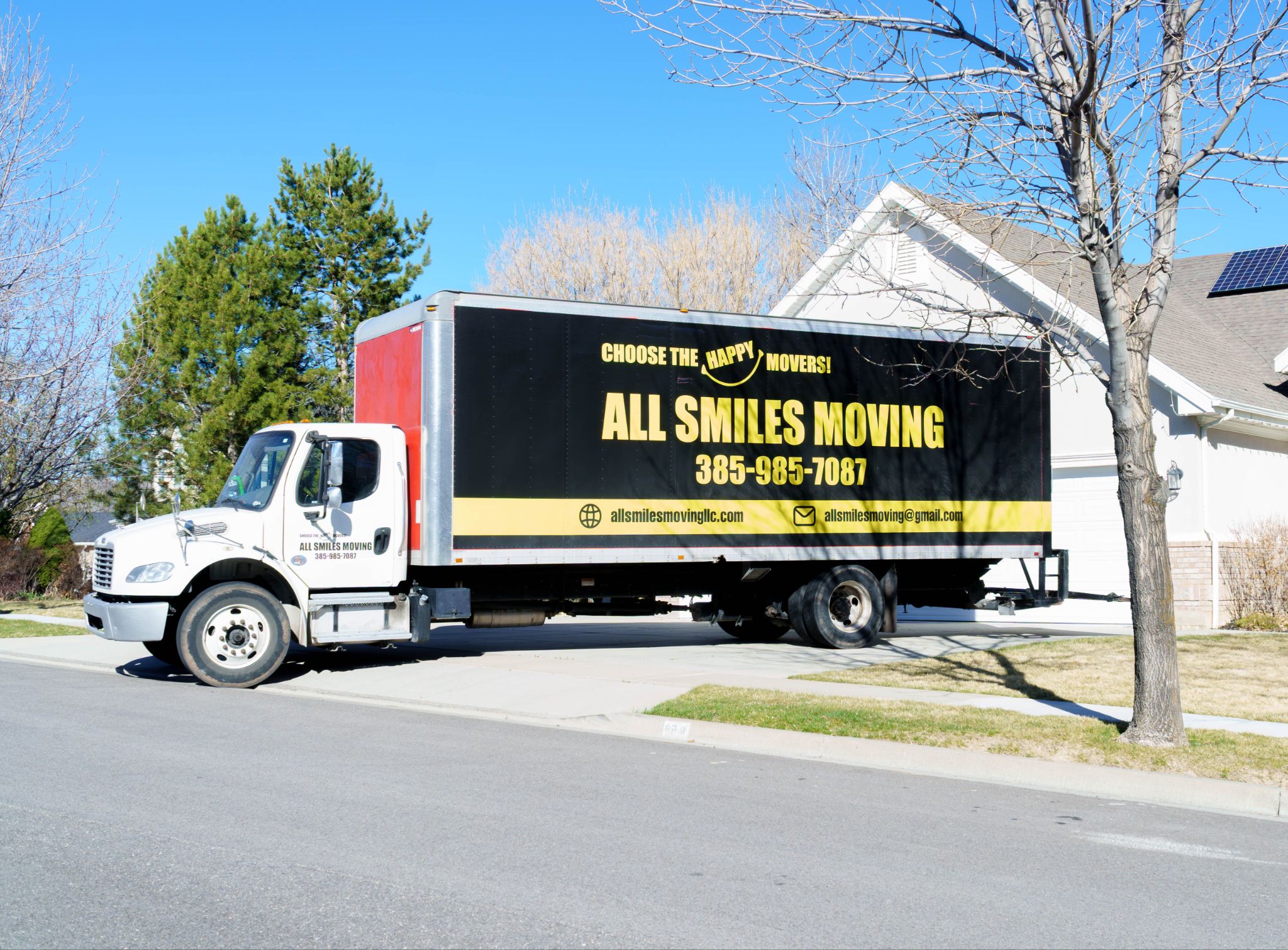 Large All Smiles Moving truck parked on a residential driveway in front of a house.